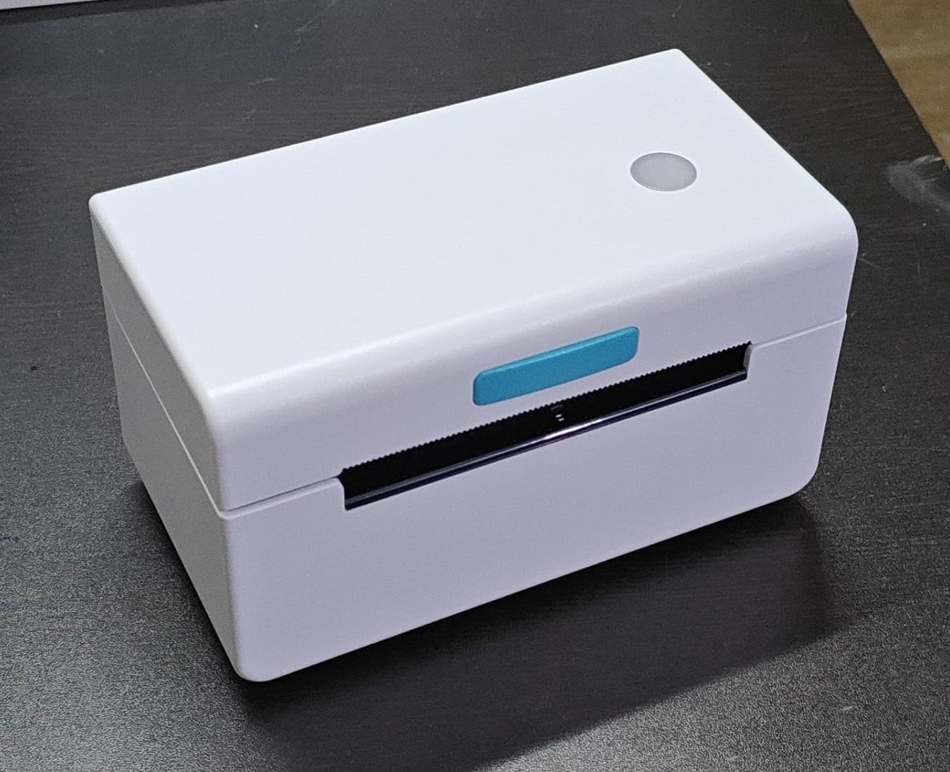 The KUPIS KP410 4x6 Shipping Label Printer from KUPIS, a compact white thermal printer with a round button on top and front slot for quality prints, elegantly adorns the dark surface.